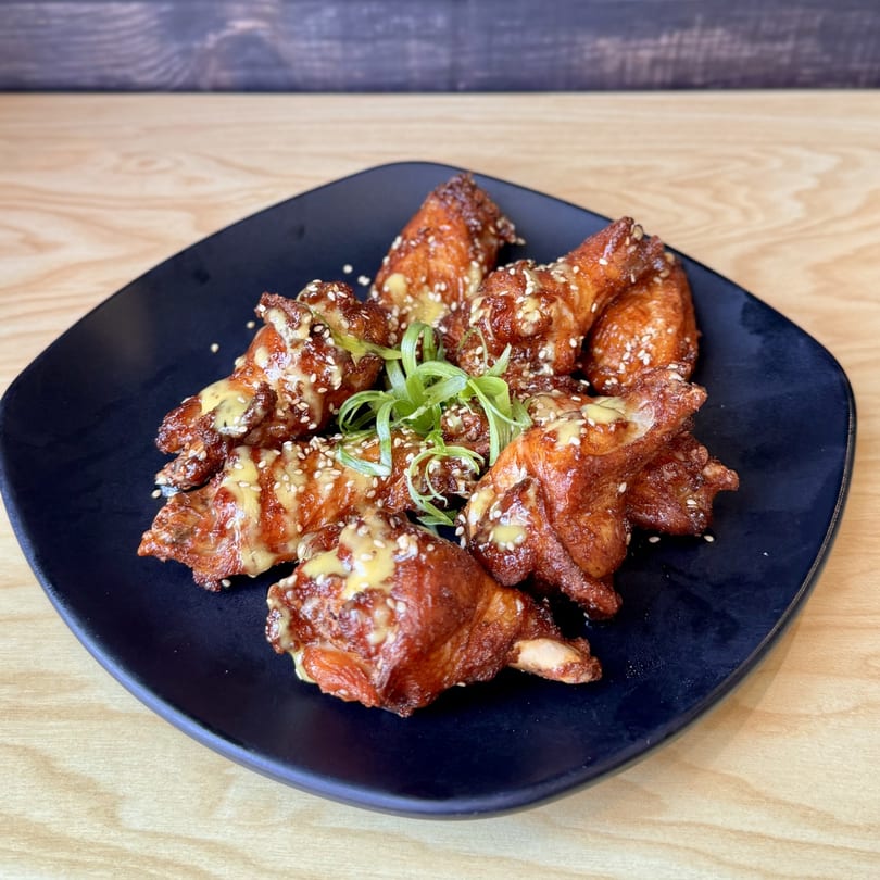 Crispy Korean-fusion chicken wings with sesame seeds, mustard drizzle, and green onions on a dark plate.