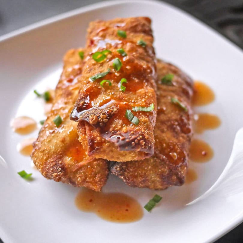 Crispy Korean-fusion egg rolls drizzled with sweet chili sauce and garnished with green onions.