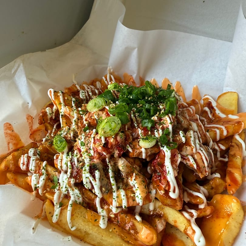 Korean-fusion fries from The District Eatery, topped with chicken, sauces, green onions, and sesame seeds.