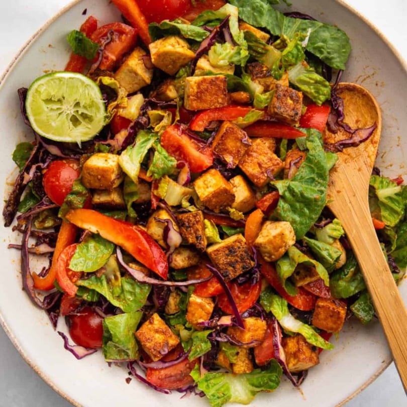 A vibrant Korean-fusion salad with crispy tofu, red peppers, cabbage, and a lime wedge.